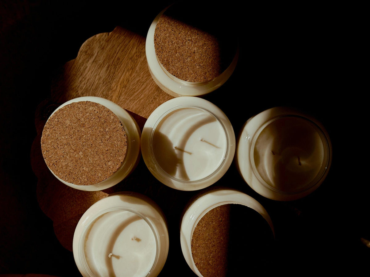 Five open white candles with cork stoppers arranged on a dark wooden surface under dramatic warm lighting.
